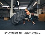 Fit female athlete working out with a huge tire, turning and flipping in the gym. Crossfit woman exercising with big tire.