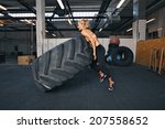 Fit female athlete flipping a huge tire. Muscular young woman doing crossfit exercise at gym.