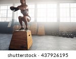 Shot of a young woman jumping onto a box as part of exercise routine. Fitness woman doing box jump workout at crossfit gym.