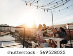 Outdoor shot of young people toasting drinks at a rooftop party. Young friends hanging out with drinks.