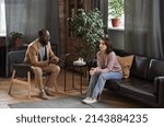 Small photo of Despondent young woman sitting on sofa and listening to psychologist at individual therapy