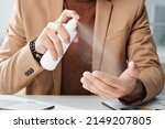 Close-up of unrecognizable office worker in jacket cleaning hands with antiseptic at workplace