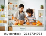 Young beautiful black mother in apron using knife while teaching son to carve Halloween pumpkin