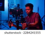 Young African American camera operator shooting on professional camera in dark studio