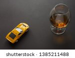 A glass of cognac and a metal toy sports car of yellow color. Still life. Dark background	