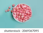 Flat lay photo of sweet pink candy (cherry, strawberry, bubble-gum flavor) popcorn in a bowl at blue background.