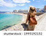 Summer holiday in Italy. Back view of young woman with hat and backpack in Gallipoli village, Salento, Italy.