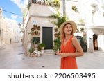 Summer holiday in Italy. Attractive young woman with hat and orange dress visiting historic cozy picturesque village of Apulia, Italy.