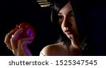Small photo of playful lewd woman with black hair is holding apple of temptation, showing her tounge
