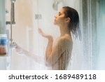 Morning shower.Taking rejuvenating cold shower.Self care moment.Everyday personal hygiene.Unfocused woman showering in glass shower with strong pressure water stream.Focus on drops