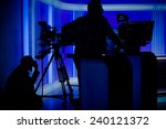 Cameraman silhouettes on a live studio news stage.Professional cameraman with headphones with camcorder in television news broadcast.Camera operators working with big broadcasting cameras
