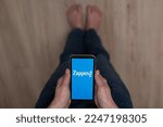 Small photo of December 3, 2022 Almaty Kazakhstan: Barefoot woman holding smartphone with zappos logo.