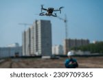 Small photo of A man in a helmet and overalls controls a drone at a construction site. The builder carries out technical oversight.