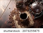 Small photo of Metallic cup and vacuum coffee maker also known as vac pot, siphon or syphon coffee maker and toasted coffee beans on rustic wooden table