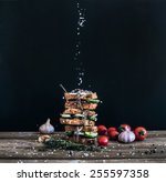 Small photo of Sandwiches with smoked meat, cucumber and herbs tied with a rope, placed one over another. Salt is being strewed on them from above on them