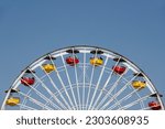 A view of a the top half of a Ferris Wheel with colorful cabins on a sunny day