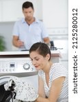 Small photo of woman holding a shrunken shirt in front of washing machine