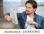 Small photo of young man sitting doing a crossword puzzle looking thoughtfully