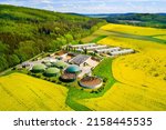 Biogas plant and farm in blooming rapeseed fields. Renewable energy from biomass. Aerial view to modern agriculture in Czech Republic and European Union. 