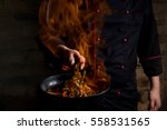 Professional chef and fire. Cooking vegetables and food over an open fire on a dark background. Hotel service photo background. Horizontal view.