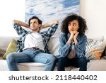 Quarrel, disagreement between a mixed race young couple. A guy and a girl, offended at each other after a quarrel, are sitting on the couch, do not talk to each other