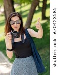 Small photo of Young woman (photographer, tourist) holds a camera and shows a gesture pollex. Selective focus.