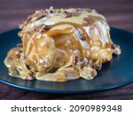 Small photo of Sweet delicious dessert a cinnamon bun sprinkled with pecans and poured with caramel topping on a black plate and a turd background.