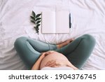 Pregnant woman with beautiful belly makes notes or check list in paper diary. Concepts of preparation for baby birth, tips for a healthy pregnancy. Minimalist style photography. Close-up, indoors.