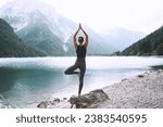 Small photo of Young woman is practicing yoga at mountain lake. Girl doing yoga on nature. Healthy lifestyles. Concept of vitality, balance, mindfulness, zen energy, calmness, relaxation.