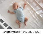 Top view wide angle sleeping newborn baby lies in a crib arms and legs outstretched, baby sleep