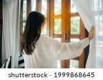 Side view of young woman wearing glasses wake up in bedroom at home or hotel, open white curtains look in window admiring to get fresh air. welcome new day morning feel positive and optimistic. 