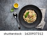 Risotto with mushrooms in a black plate over gray background, top view