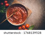 Small photo of Classic homemade Italian tomato sauce with basil for pasta and pizza in the pan on a wooden chopping board on brown background, top view.