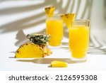 Small photo of Pineapple cocktail or juice in two glasses with ice on white background with palm leaves shadows