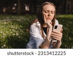 Small photo of Woman holding a phone while holding her hand on chin. Expressive student thinking outside in campus - Woman in doubt with smartphone in her palm, think about reading information, search solution.