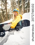 Small photo of Caucasian woman snowboarder holds snowboard on beautiful snowy forest background in sunny day.