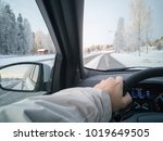 Caucasian man is driving on a wintry asphalt road. Snow covered ground, red cottage on side of the road. Mirror reflecting back the highway. Focus point on the trees in front, road composed in middle