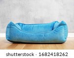 Empty turquoise blue bed for domestic pets made from soft fabric, setting on wooden floor. Indoors, light gray wall background, copy space.