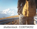 Small photo of Close-up of a backpack in the back of a male traveler walking along a country road in the background of a mountain. Copy the blank for the dieser. Journey