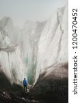 Small photo of A free climber with an ice ax in his hand stands at the foot of the Great Glacier next to an epic crack in the fog in the mountains. Insurmountable obstacle