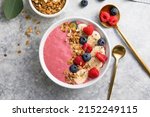 Summer acai smoothie bowls with raspberries, banana, blueberries, and granola on gray concrete background. Breakfast bowl with fruit and cereal, close-up, top view, space for text