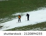 Two skiers putting on skis at the bottom of a ski slope finishng in the green valley, covered with artificial snow due to warm winter. Bottom of the Ahorn mountain, Mayrhofen, Austria