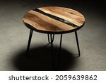 Small photo of Expensive vintage furniture. The table is covered with epoxy resin and varnished. Luxury quality wood processing. Wooden table on a dark background. A black epoxy river in a round tree slab.