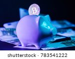 Bitcoin in the slot of a piggy bank standing on a pile of euro bills. Conceptual closeup image for worldwide cryptocurrency and digital payment system. Unique blue/violet lighting. Side view.