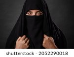 Close up portrait of young, adult woman in black burqa  with hidden face, isolated on black background.