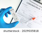 Doctor hand showing covid-19 positive test on antigen rapid test kit for coronavirus with laboratory report on table.