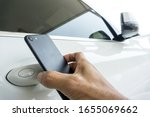 Close up of man uses a smartphone to place near to the door handle of a car for communication to lock, unlock the car.