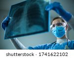 Small photo of Female pulmonologist or oncologist holding chest X-ray scan,inspecting COVID-19 patient lungs,wearing PPE uniform,Coronavirus acute respiratory new virus disease infection causing breathing problems