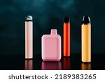 A set of colorful disposable electronic cigarettes of different shapes on a black background with smoke. Concept of modern smoking, vaping and nicotine.