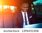 Handsome successful rich african american business men entrepreneur in a stylish black suit and tie sitting in a luxury car and works with laptop. concept of luck and currency market stock exchange